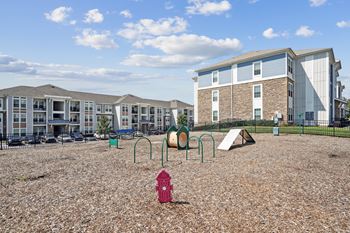 A playground with a red fire hydrant in the foreground and apartment buildings in the background.